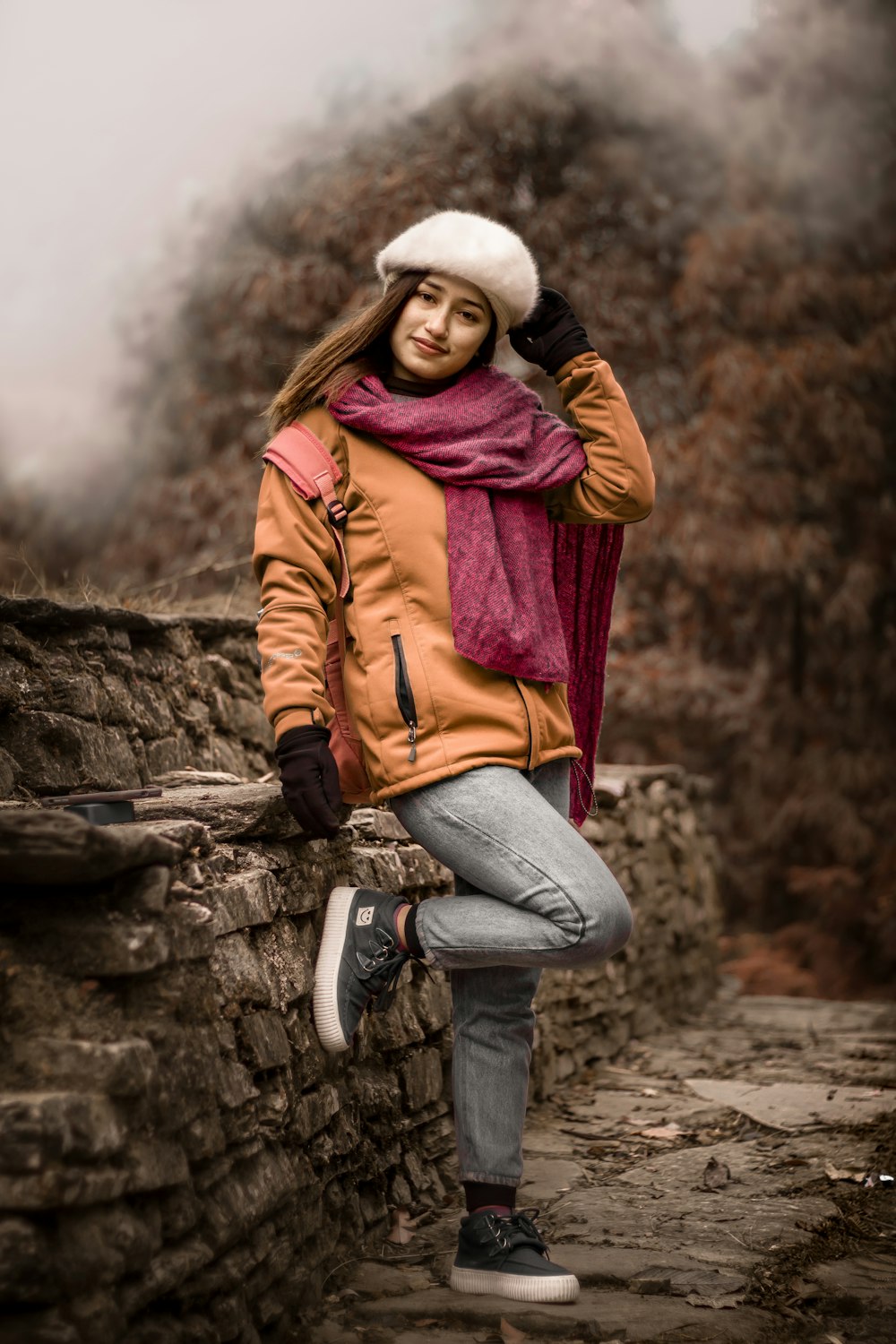 woman in brown jacket and blue denim jeans sitting on rock