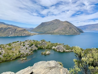 green and brown mountain beside lake under blue sky during daytime