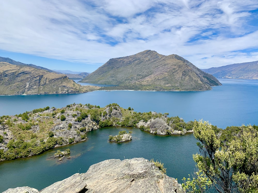 green and brown mountain beside lake under blue sky during daytime