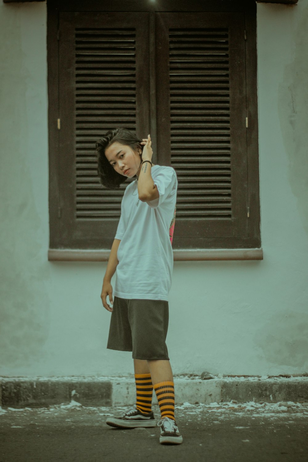 girl in white t-shirt and black shorts standing beside brown wooden door