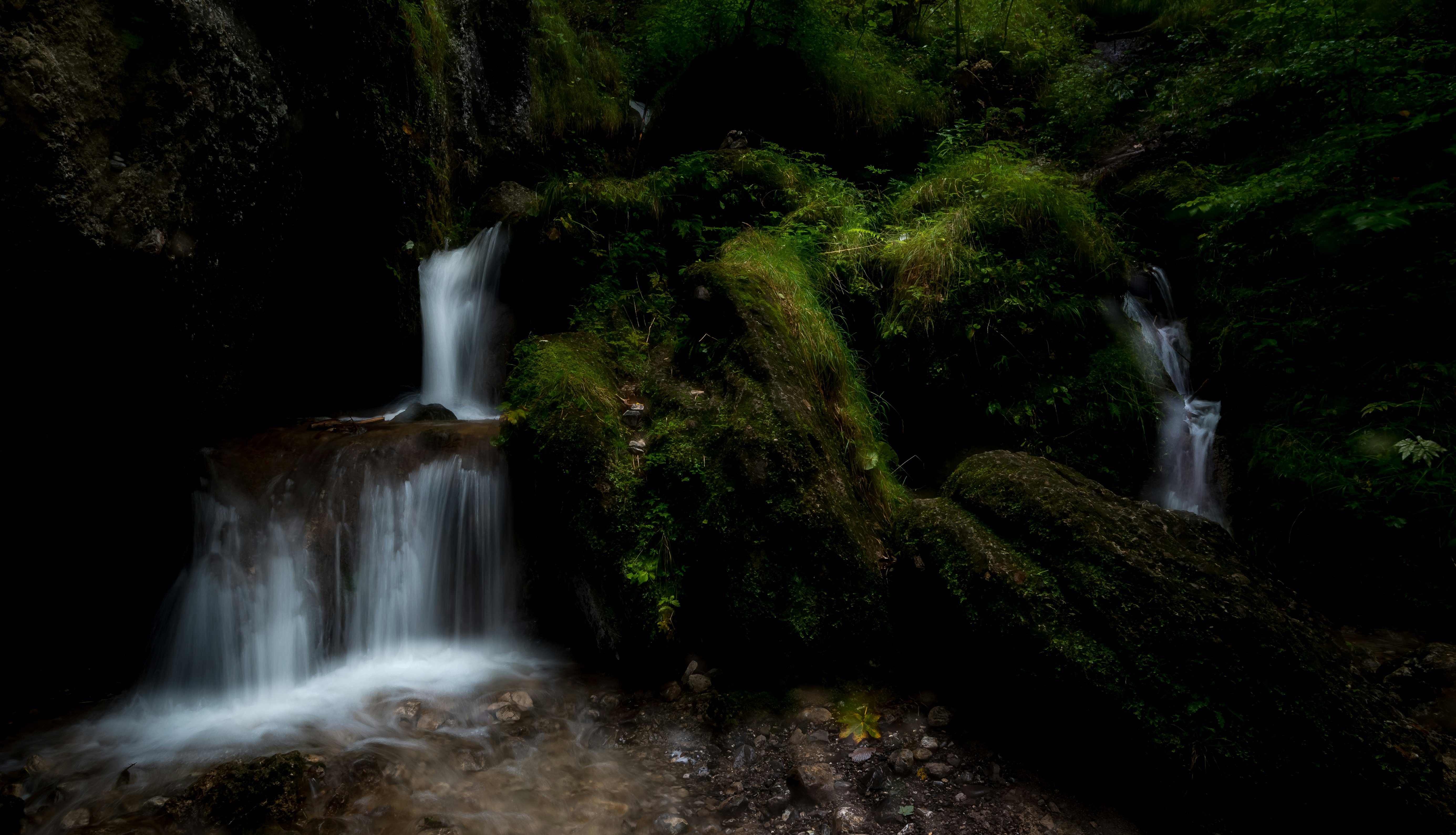 water falls in the middle of green moss covered rocks