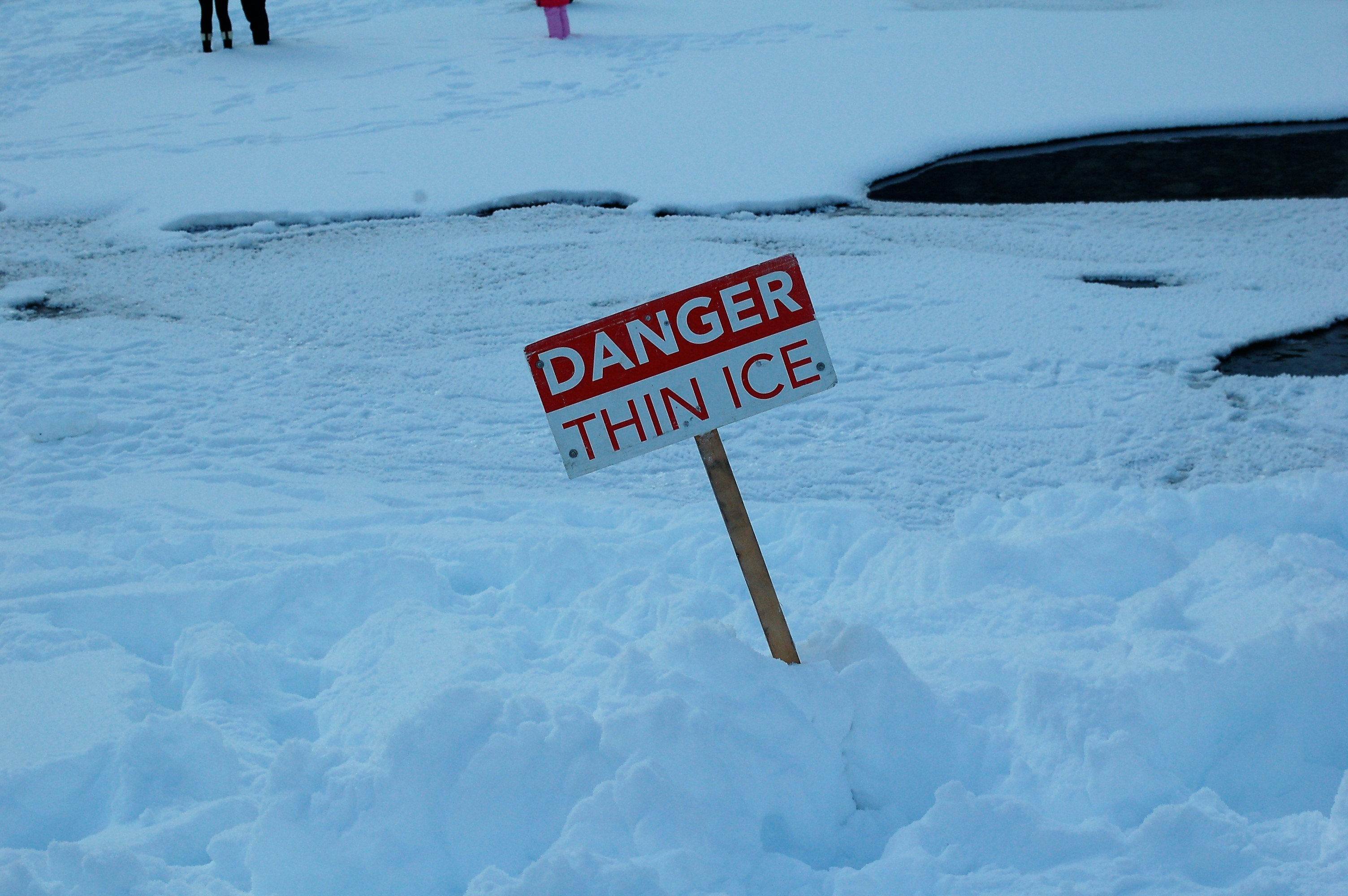 white and red open signage on snow covered ground warning of dangers of ice