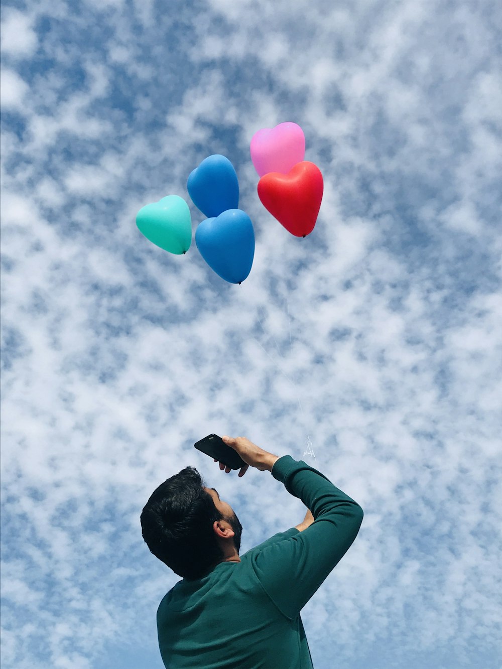 man in black jacket holding pink blue balloons