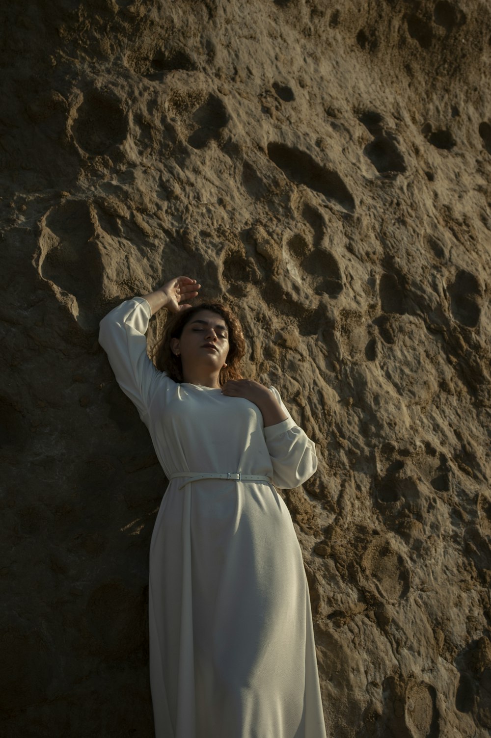 woman in white long sleeve dress standing on brown rock