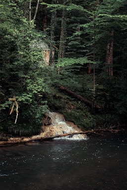 Wooden cabin nestled beside a natural waterfall at sunset.