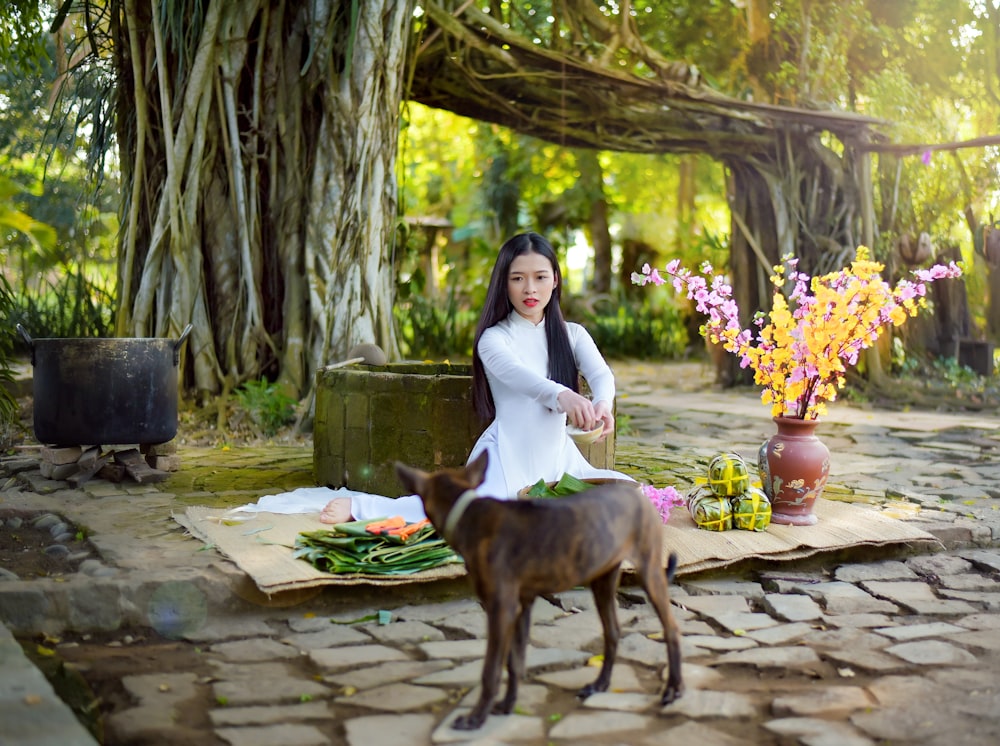 woman in white long sleeve shirt sitting beside brown short coated dog