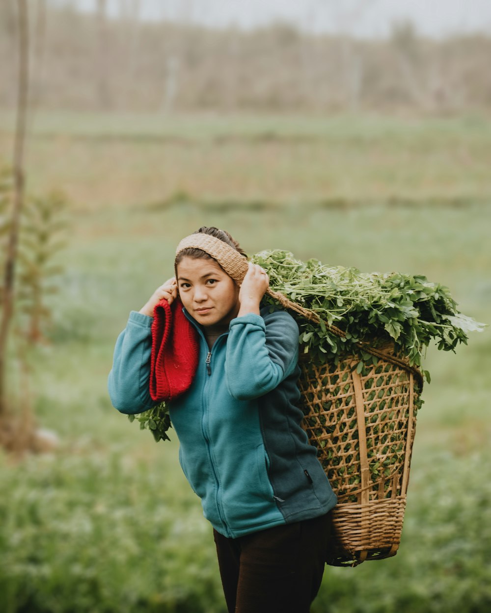 woman in blue long sleeve shirt carrying brown woven basket with green leaves