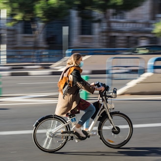 woman in brown jacket riding on bicycle on road during daytime