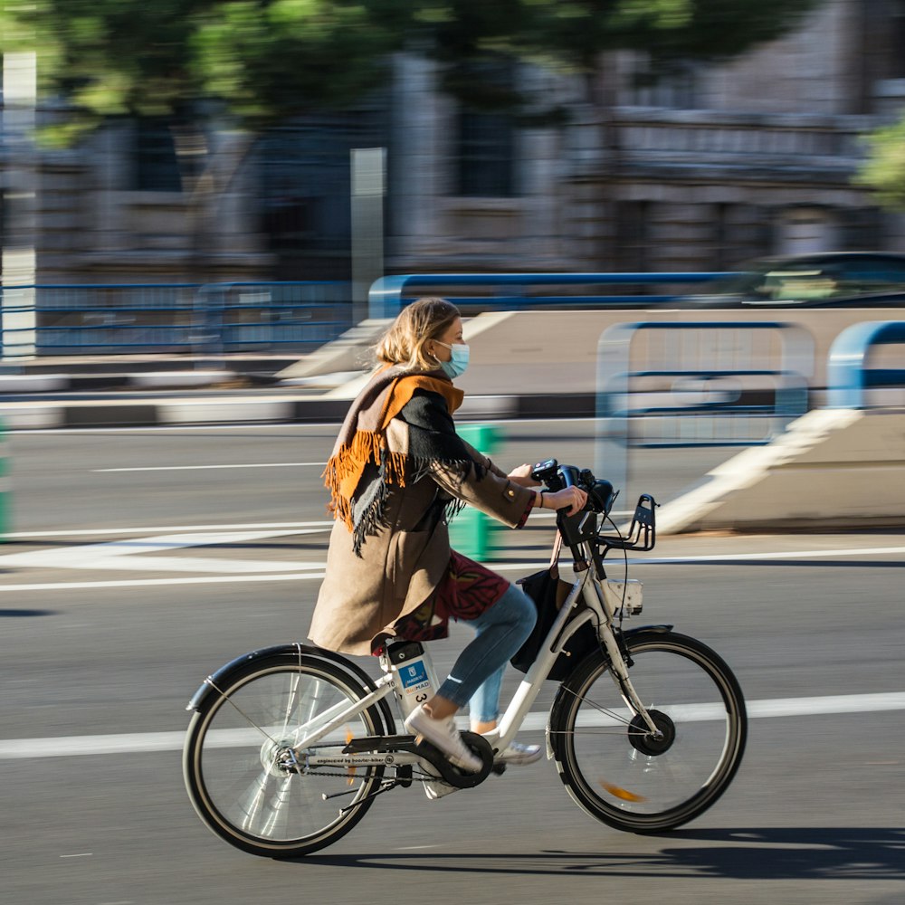 Donna in giacca marrone che cavalca sulla bicicletta sulla strada durante il giorno