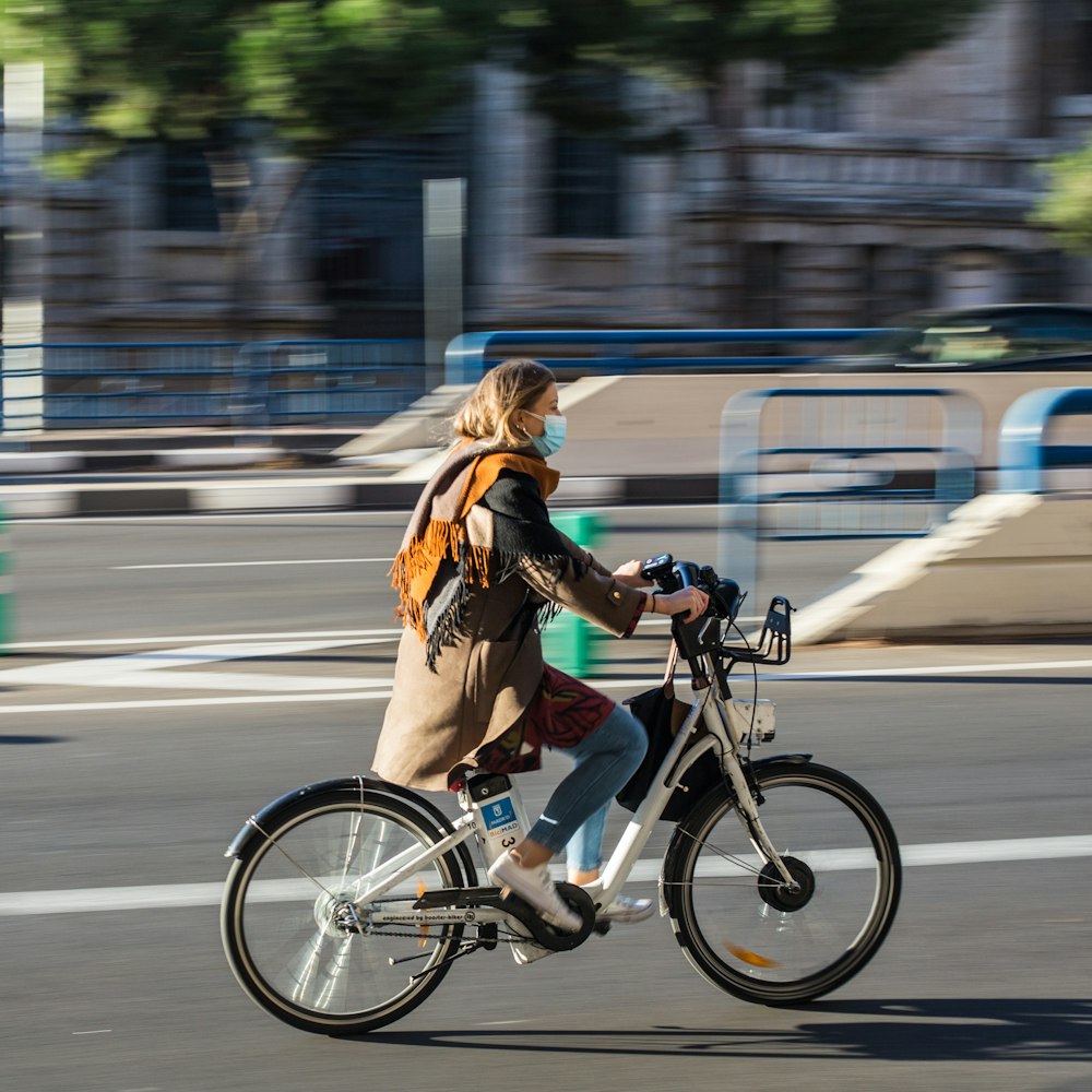 Mujer con chaqueta marrón montando en bicicleta en la carretera durante el día