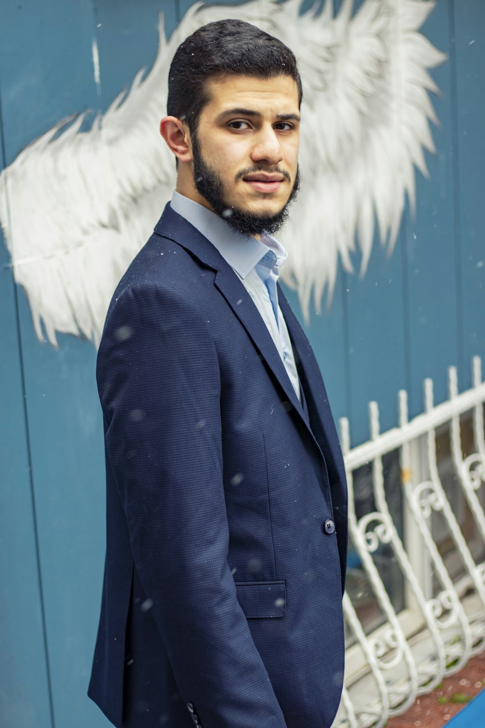 man in black suit jacket standing near blue wall