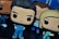 Vinyl figurines with oversized heads and cartoonish features dressed in blue clothing, standing on a dark surface. The figures exhibit exaggerated expressions and styles, hinting at character portrayals. Additional figures can be seen partially in the background.