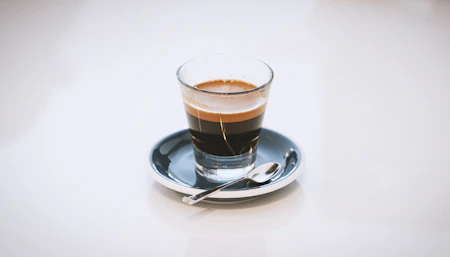 An espresso in a small glass on a blue saucer, white background