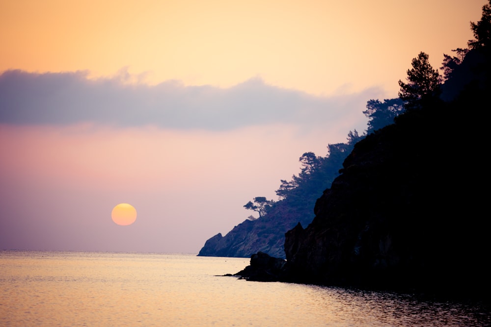 silhouette of mountain near body of water during sunset