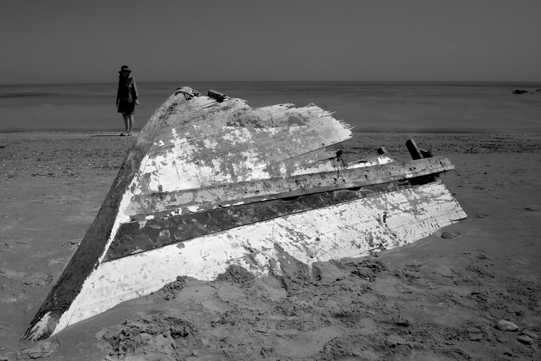 grayscale photo of man and woman standing on rock formation near sea