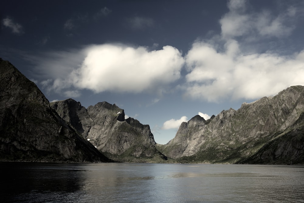 body of water near mountain under white clouds and blue sky during daytime