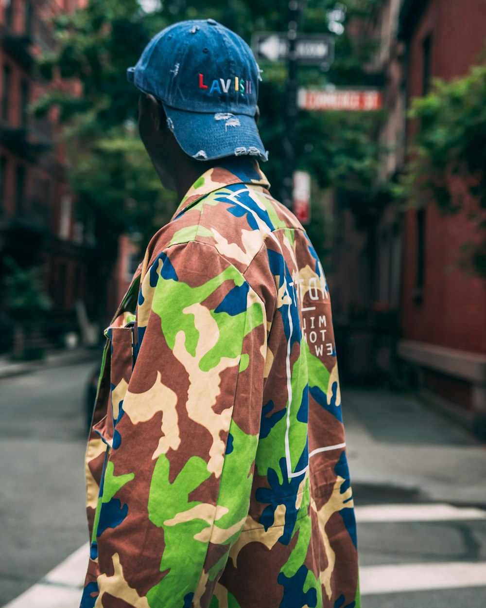 man in green brown and black camouflage jacket standing on sidewalk during daytime