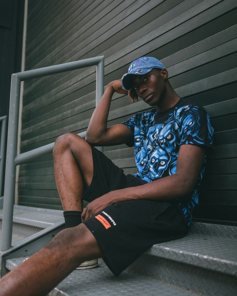 man in blue and white floral shirt and black shorts sitting on gray wooden stairs