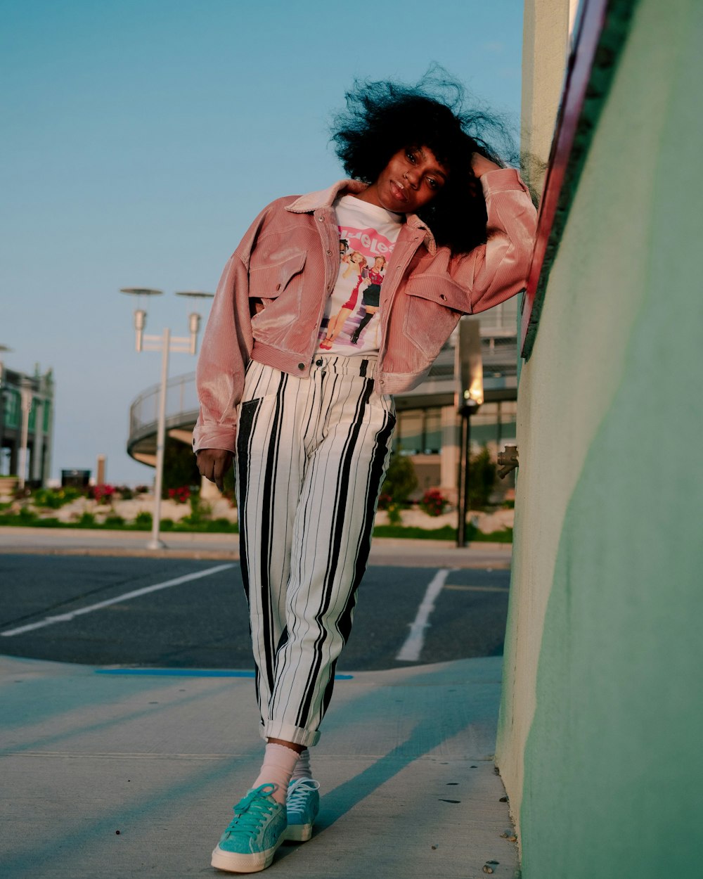 woman in pink jacket and black and white striped pants standing on gray concrete floor during