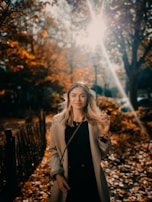 A model in a tailored camel coat with a soft scarf, walking through an autumn park with golden leaves.