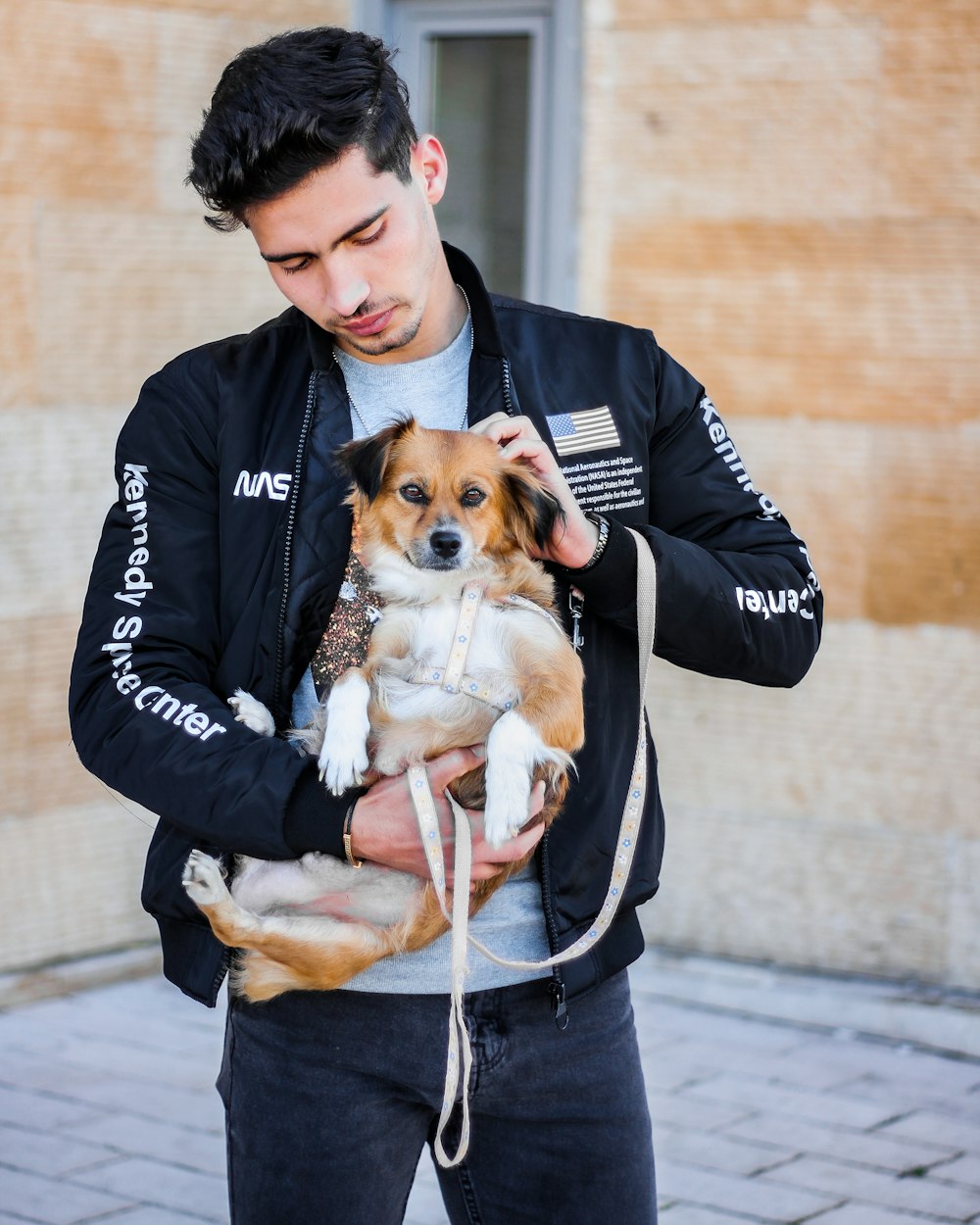 man in black jacket carrying brown and white short coated dog