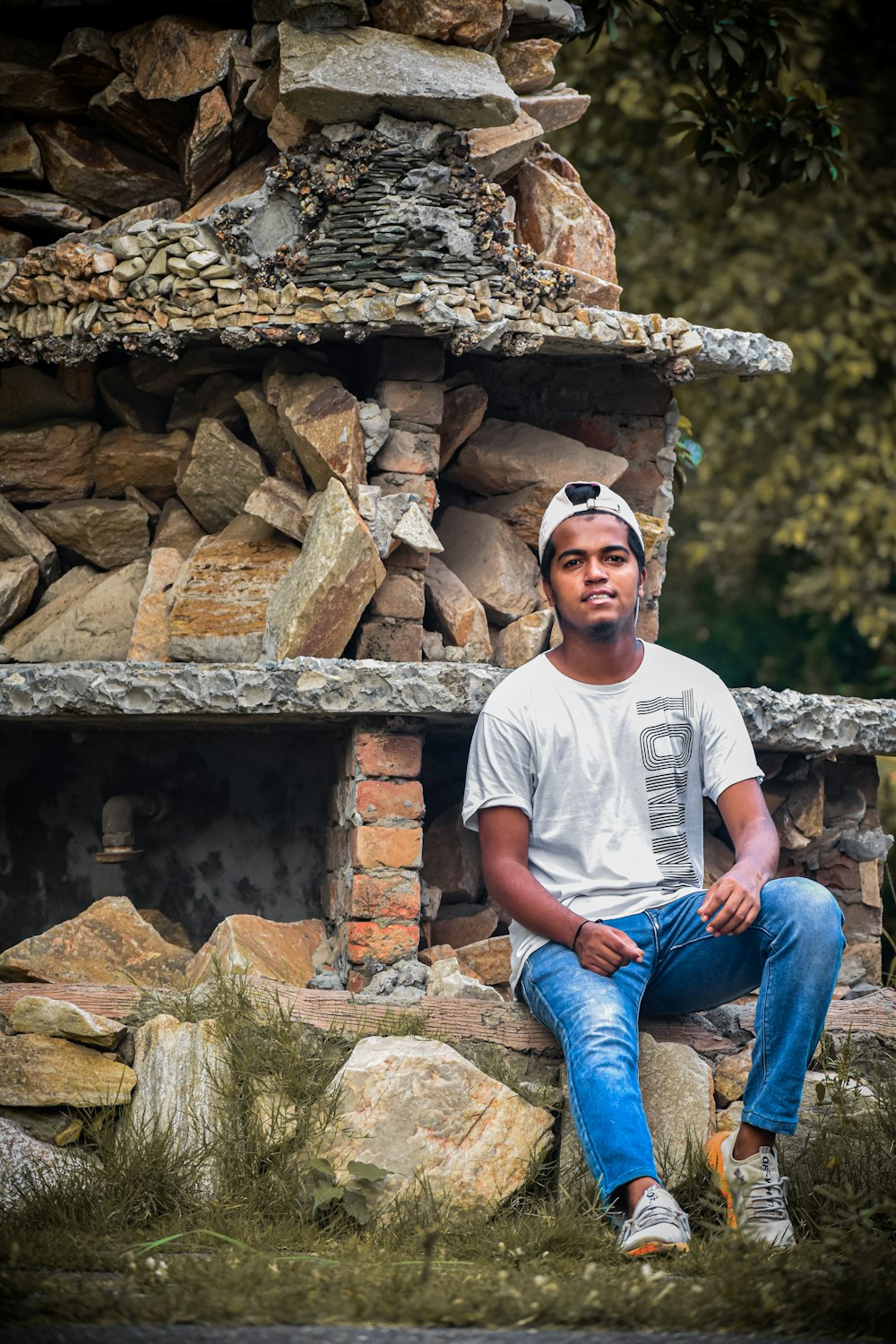 uomo in t-shirt bianca girocollo e jeans denim blu seduto sulla roccia marrone durante