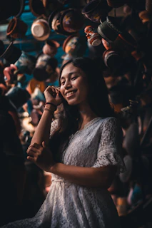 A joyful woman wearing an eleen dress, standing in a sunlit room filled with vibrant ceramic pots.