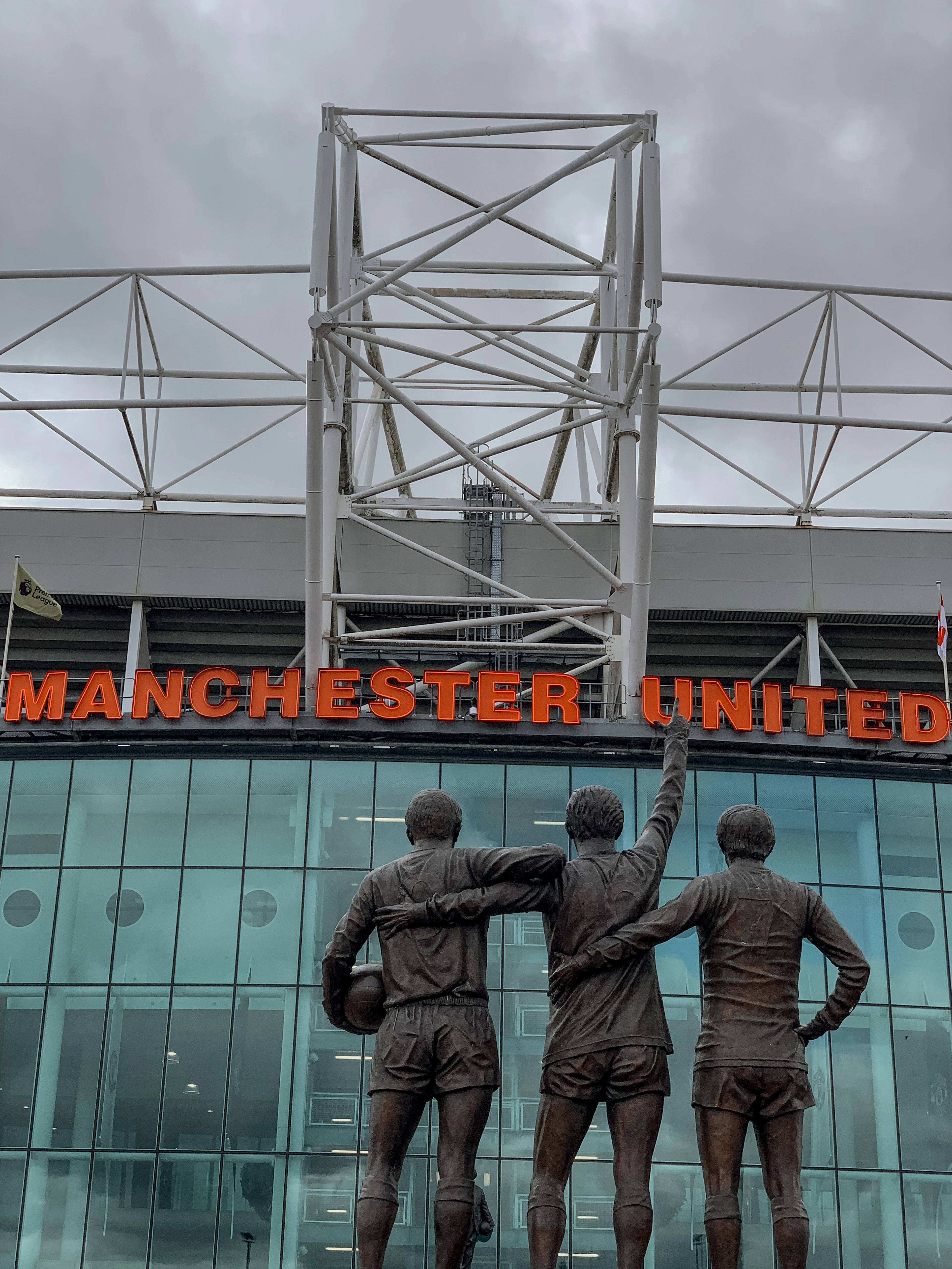 Bronze statue of three footballers below a Manchester United stadium sign