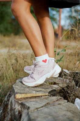person wearing white nike sneakers standing on brown rock