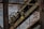 An industrial scene featuring rusted metal beams and machinery against a backdrop of a weathered brick wall. A large pulley system with visible chains is prominent, along with a sign indicating load capacity.