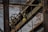 An industrial scene featuring rusted metal beams and machinery against a backdrop of a weathered brick wall. A large pulley system with visible chains is prominent, along with a sign indicating load capacity.