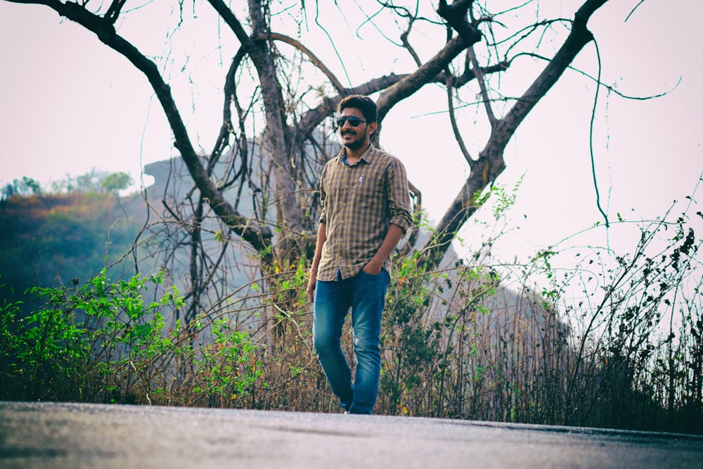 man in brown and white checkered dress shirt and blue denim jeans standing beside tree during