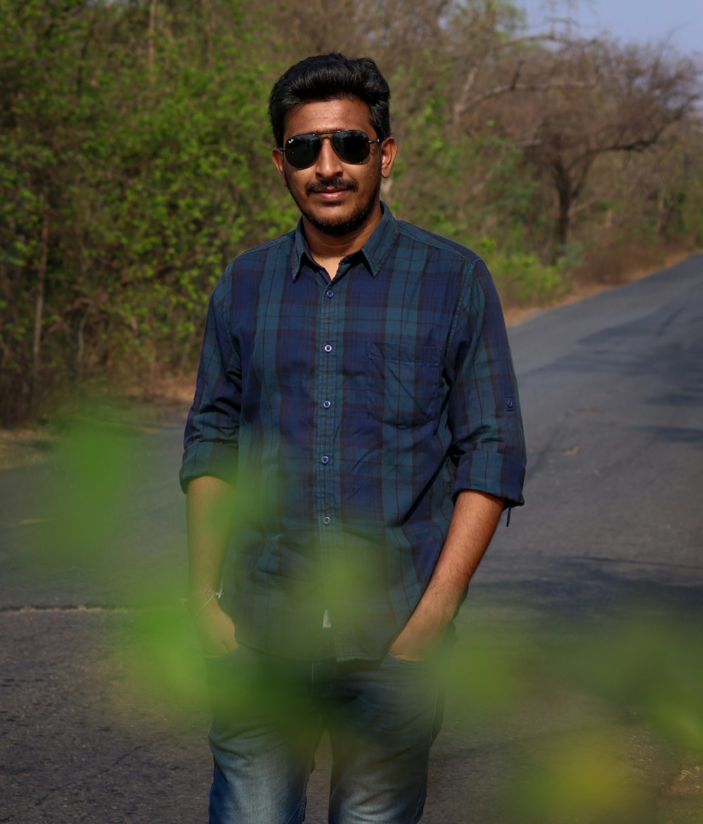 man in blue button up shirt wearing black sunglasses standing on road during daytime