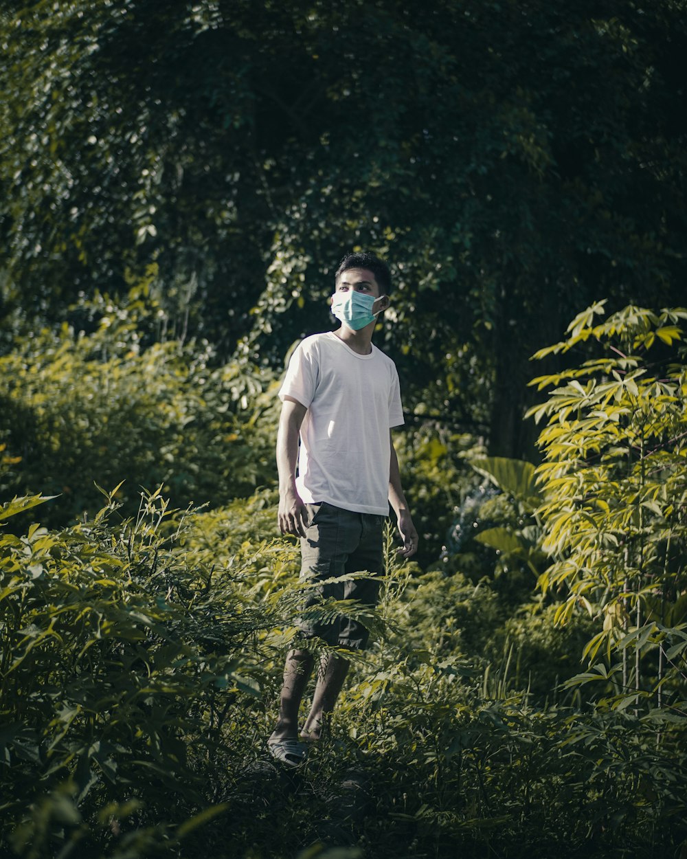 man in white t-shirt and black denim jeans wearing black headphones standing on green grass