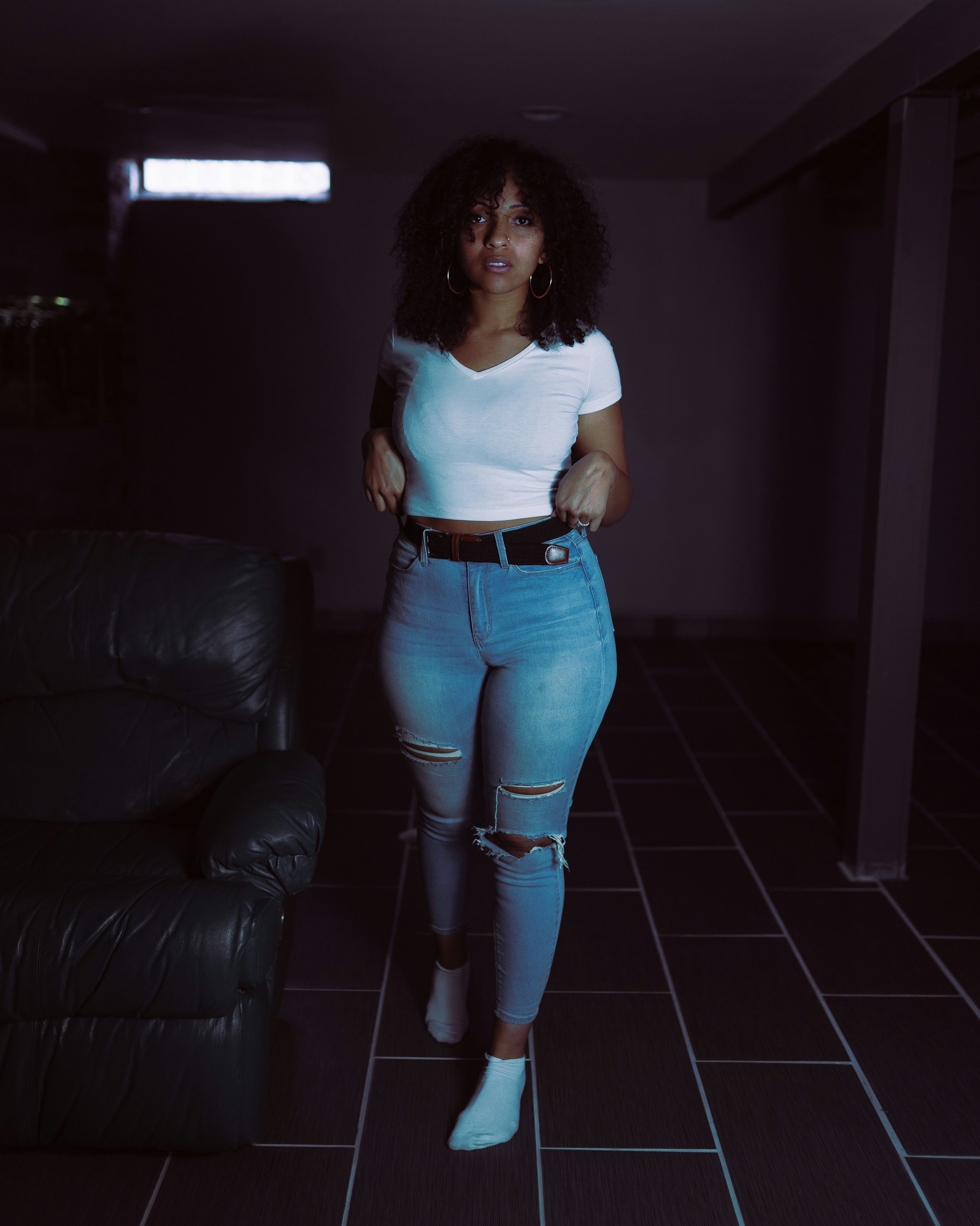 白いタンクトップと黒い革のソファの横に立っている青いデニム ジーンズの女性の写真 Unsplashで見つける青いの無料写真