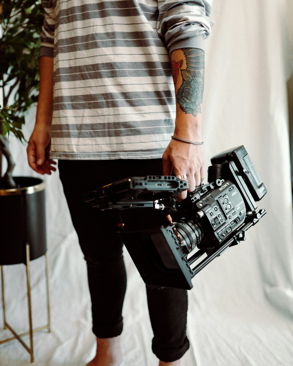 man in white and brown stripe shirt and blue denim jeans holding black and gray camera