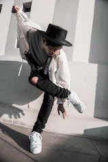 man in white dress shirt and black cowboy hat jumping on gray concrete floor during daytime