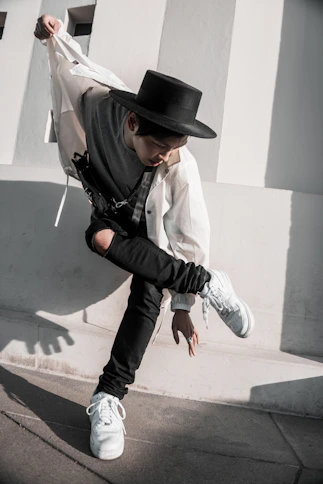 man in white dress shirt and black cowboy hat jumping on gray concrete floor during daytime