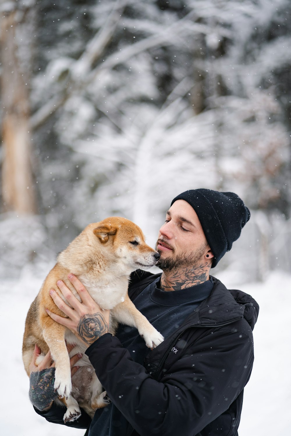 man in black jacket hugging brown and white short coated dog