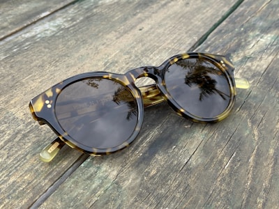 A pair of tortoiseshell sunglasses catching sunlight on a wooden table.