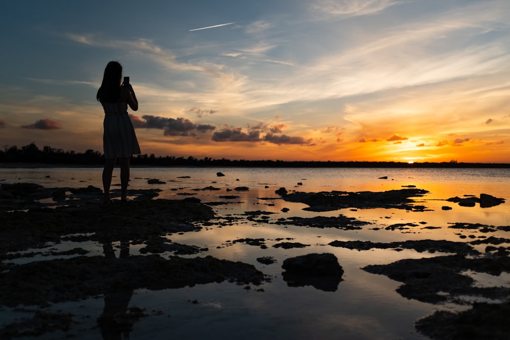 woman in black dress standing on water during sunset