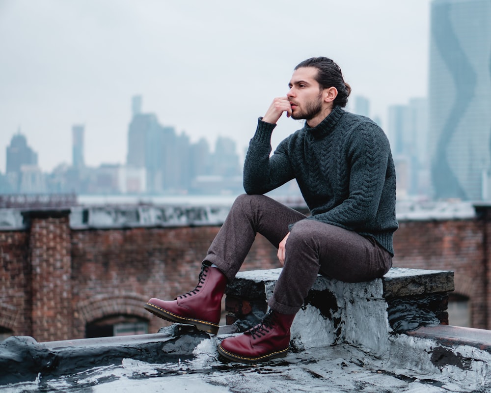 man in gray sweater and blue denim jeans sitting on gray concrete bench during daytime