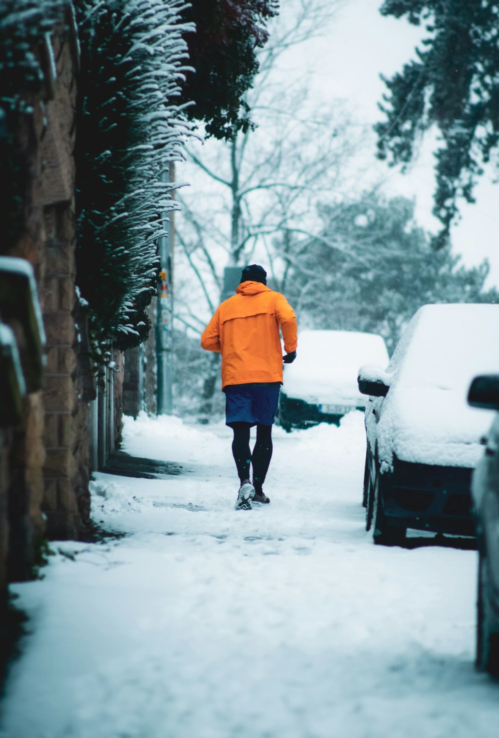 日中に雪に覆われた小道を歩くオレンジ色のパーカーを着た人