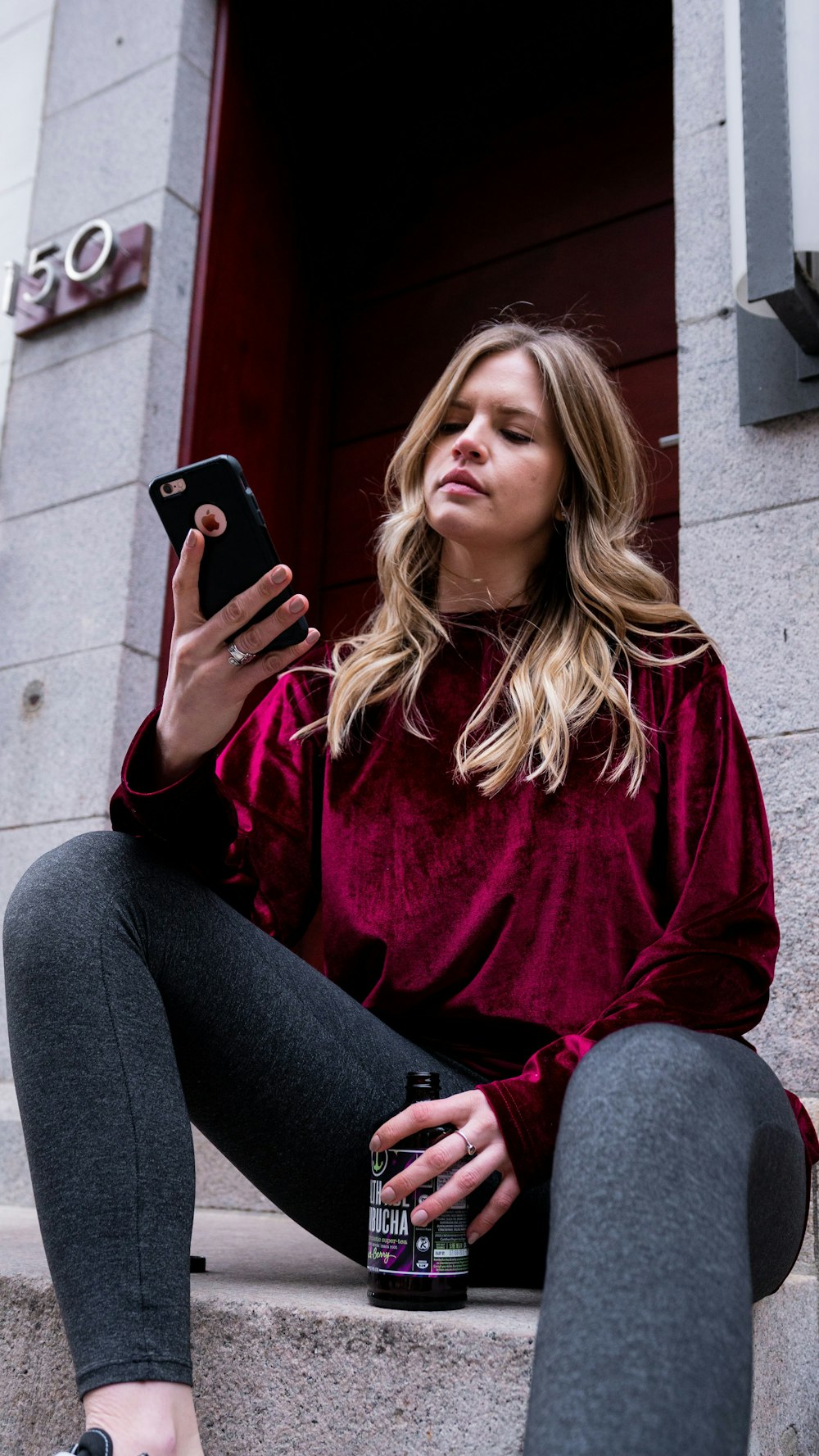 woman in red sweater and gray pants holding black smartphone