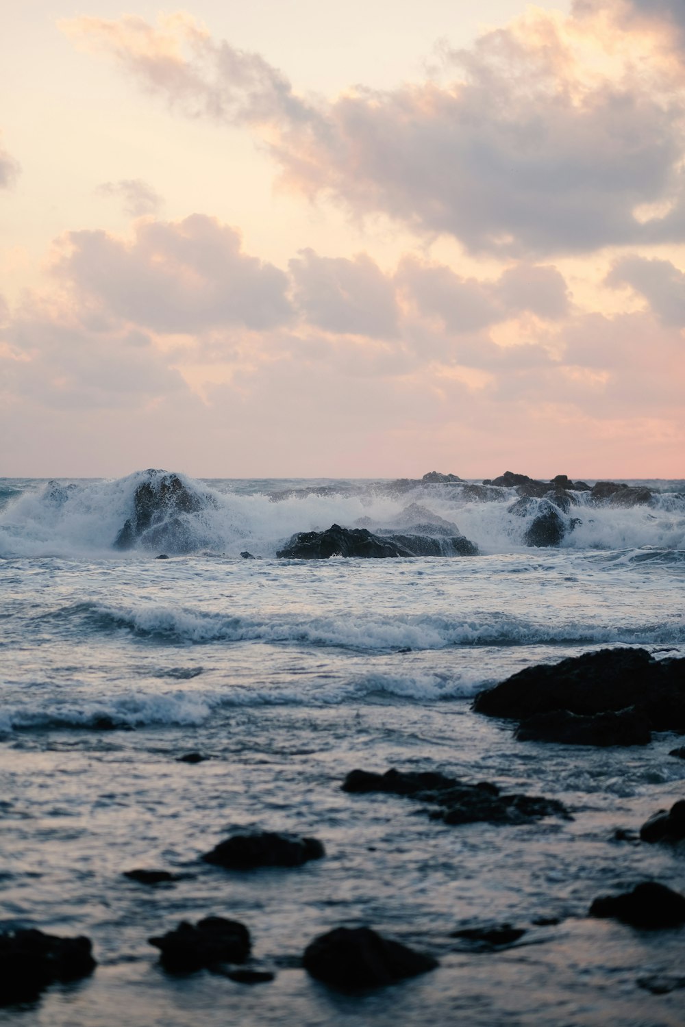 ocean waves crashing on rocks under white clouds during daytime