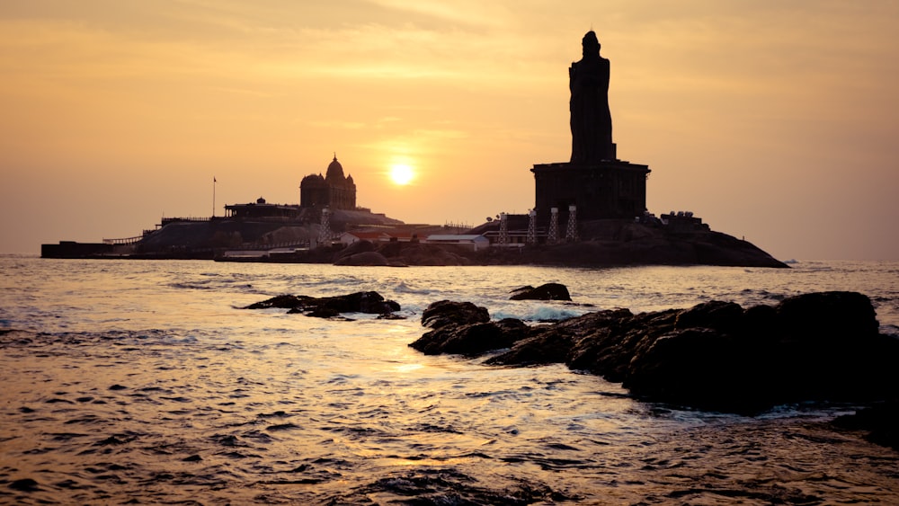 silhouette of building on rock formation near body of water during sunset