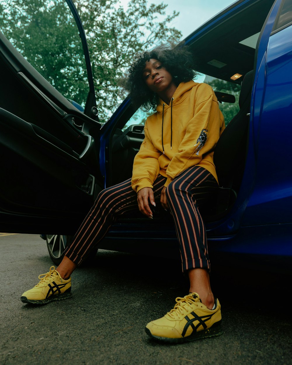 woman in yellow jacket and black and white striped pants sitting on blue car