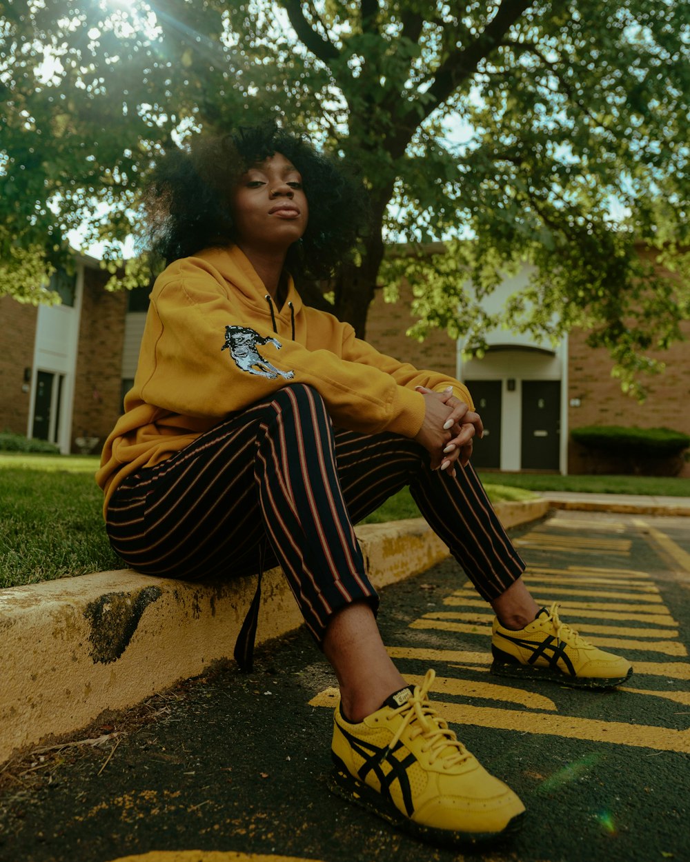 woman in yellow hoodie and black and white striped pants sitting on brown concrete bench during