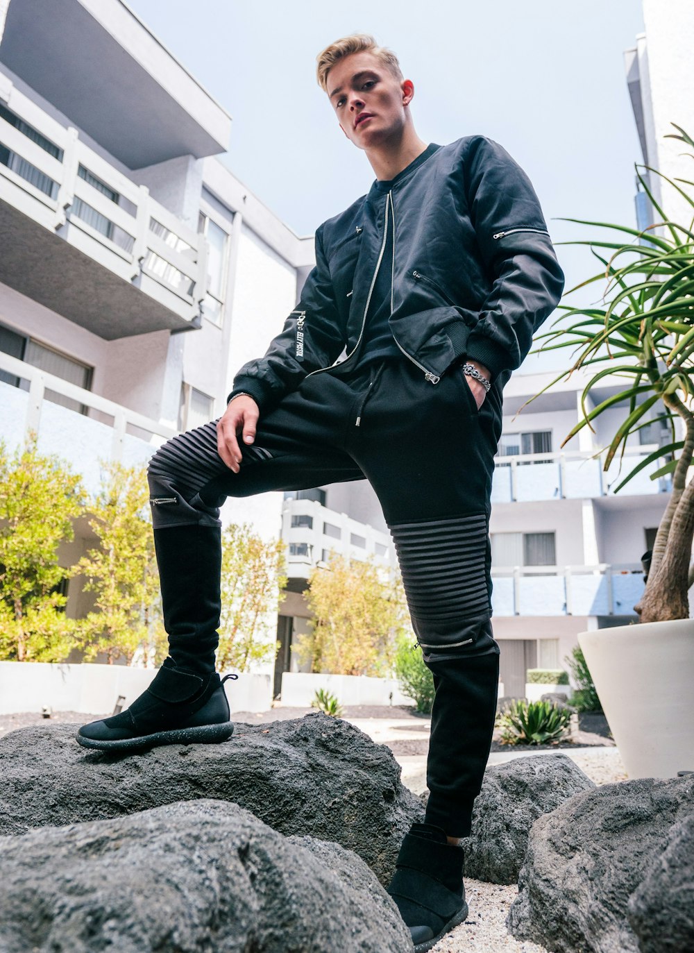 man in black leather jacket and black pants standing on gray rock