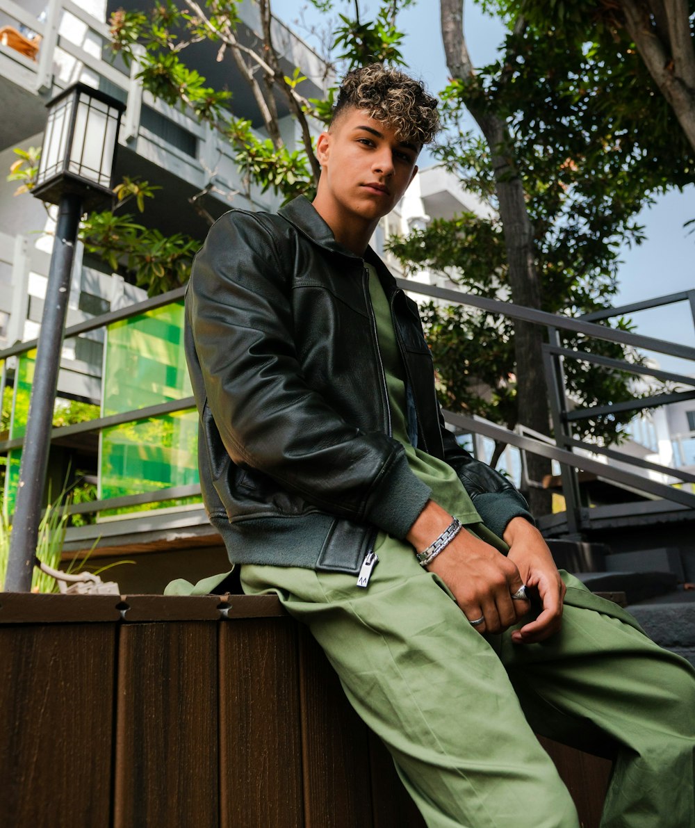 Man in black leather jacket and green pants sitting on brown wooden bench  photo – Free Apparel Image on Unsplash